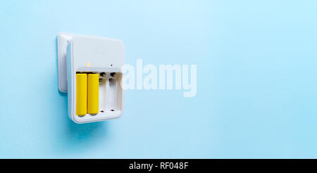 Foto di caricabatterie con due batterie giallo vuota su sfondo blu Foto Stock