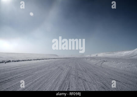 Una strada di ghiaccio che conducono verso la neve sulle colline coperte con un parziale sundog situato vicino alla comunità di Cambridge Bay, Nunavut, Canada Foto Stock