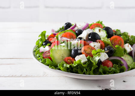Fresca insalata greca nella ciotola con il nero oliva,il pomodoro,formaggio feta, cetrioli e cipolle bianche su un tavolo di legno. Foto Stock