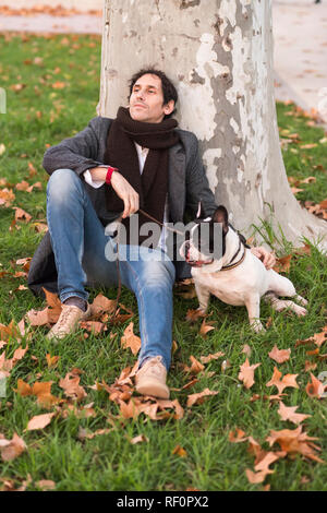 Scena urbana. Uomo vestito in seduta informale sul prato accanto al suo cane Foto Stock