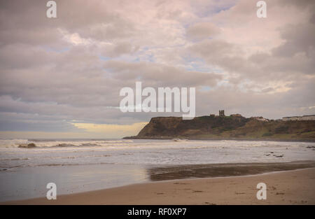 North Beach, Scarborough. Ruggito onde verso la spiaggia e una capezzagna è in background con un castello in rovina la skyline. Cloud pesante sopra. Foto Stock