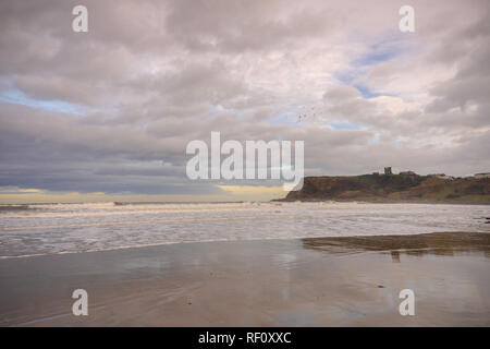 North Beach, Scarborough. Ruggito onde verso la spiaggia e una capezzagna è in background con un castello in rovina la skyline. Cloud pesante sopra. Foto Stock