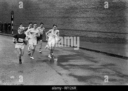 Degli anni Cinquanta, storico dilettante guide maschio in competizione in una esecuzione di corsa su strada sul bagnato le strade di una città, England, Regno Unito Foto Stock