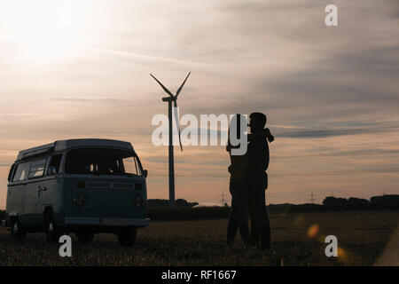 Coppia giovane kissing a camper van al tramonto con la turbina eolica in background Foto Stock