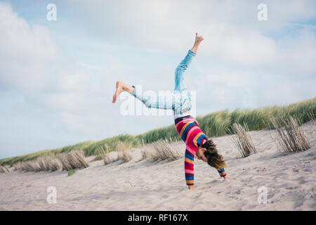 Donna matura divertendosi, cartwheeling sulla spiaggia Foto Stock