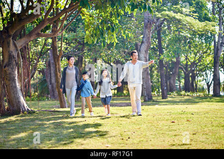Famiglia asiatica con due figli che camminano mano nella mano all'aperto nel parco. Foto Stock