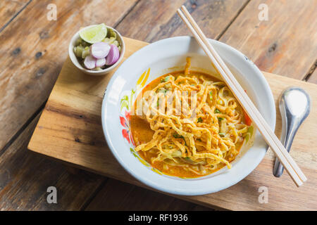 Salsa speziata zuppa di noodle (Khao soi) con carne di pollo speziati e latte di cocco sulla tavola di legno. Cibo tailandese cucina stile settentrionale di Chiang Mai. Foto Stock