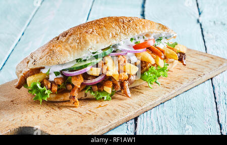 Deliziosi gyros greco burger con carne arrosto affettata da un kebab, patatine fritte, insalate fresche passamaneria su un cilindro di pane croccante servita su una scheda Foto Stock