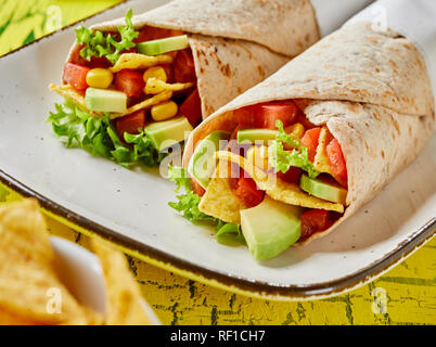 Deliziosa tortilla avvolge con fresche avocado, insalata ingredienti e nachos su una piastra rettangolare per uno spuntino in una vista ravvicinata Foto Stock