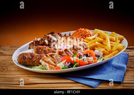 Piatto pieno di cucina greca souvlaki con patatine fritte e insalata su sfondo di legno Foto Stock