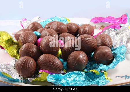 Pila di cioccolato non confezionate le uova di pasqua con il colorato involucro di carta metallizzata che lo circonda su uno sfondo bianco. Foto Stock