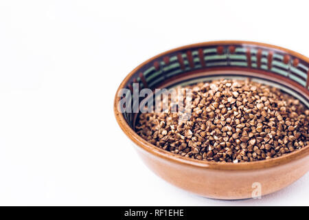 Raw a secco i chicchi di grano saraceno in marrone vaso in ceramica bianca su sfondo di legno Foto Stock