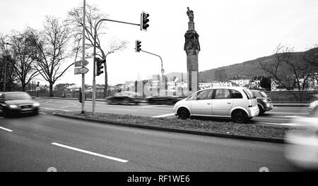 TRIER, Germania - Feb 21, 2015: Automobili e la statua dell'Imperatore Costantino tenendo una corona con una croce in cima ad una colonna ai piedi della Kaiserstrasse strada imperiale sul fiume Moselle - bianco e nero Foto Stock