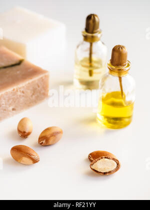 Bottiglie con olio di argan dadi. Mezzi di cosmetici. Prodotto alimentare. Vaso con olio di argan e sapone artigianale sullo sfondo isolato. Foto Stock