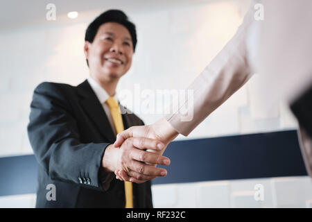 Stretta di mano tra felice Asian Manager e imprenditrice ispanica in Office Foto Stock