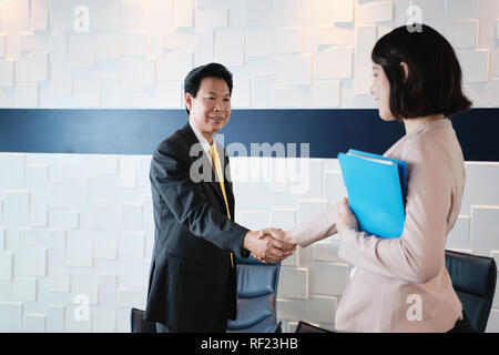 Stretta di mano tra felice Asian Manager e imprenditrice ispanica in Office Foto Stock