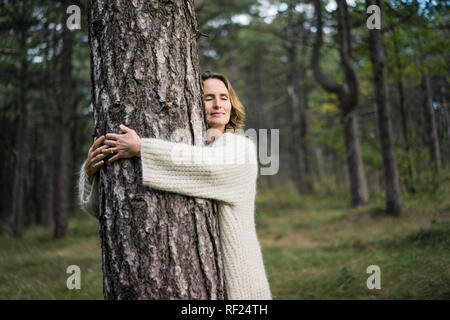 Donna abbracciando albero nella foresta Foto Stock