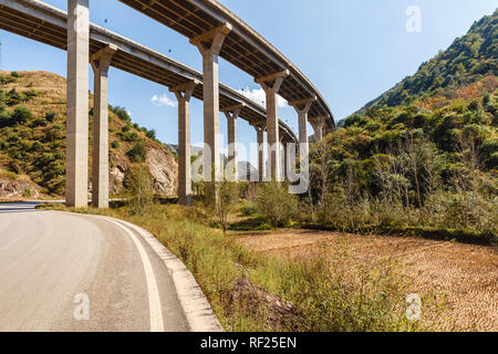 Una strada asfaltata in montagna passa sotto un'autostrada cavalcavia, Cina Foto Stock