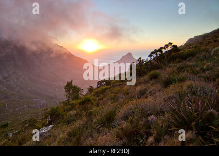A sunset hike up Devil's Peak afords incredible views as the sun dips below the Atlantic Ocean horizon, Cape Town, Western Cape Province, South Africa Foto Stock