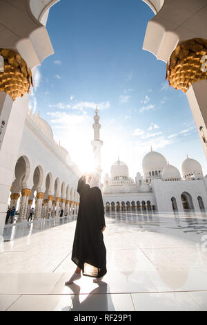 Tradizionalmente condita arabo donna vestita di nero burka wisiting Sheikh Zayed Grande Moschea di Abu Dhabi, negli Emirati Arabi Uniti. Foto Stock