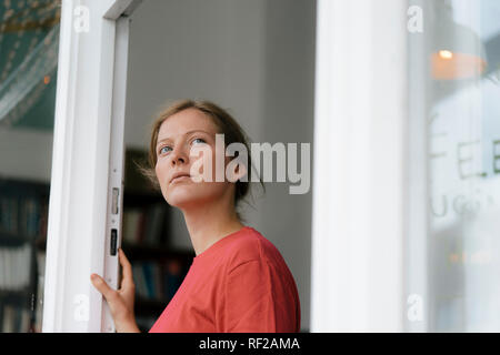 Giovane donna alla porta francese in una caffetteria guardando intorno Foto Stock