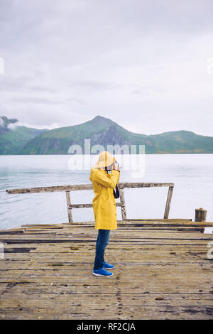 Norvegia, Senja, uomo in piedi su un molo sgangherato presso la costa di scattare una foto Foto Stock