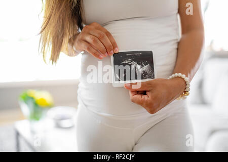 Close-up della donna incinta contiene foto di ultrasuoni al suo ventre Foto Stock