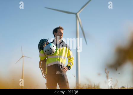 Il tecnico in piedi in un campo di una fattoria eolica con arrampicata attrezzature Foto Stock