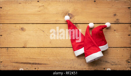 Una immagine di tre rossi Santa Claus cappelli con sfondo di legno Foto Stock