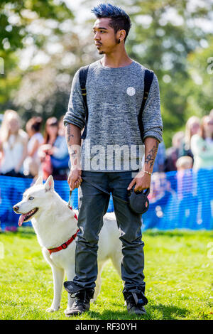 Un giovane uomo in piedi con il suo cane husky nel parco di un dog show Foto Stock