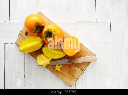 Intero e fette Kakis e frutti a stella sul pannello di legno Foto Stock