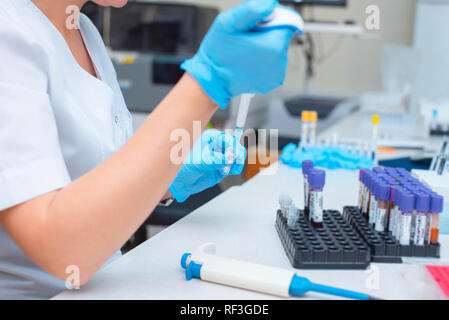 Esame del sangue in laboratorio. Assistente di laboratorio lavora con il distributore. Tubi a vuoto con il sangue. Foto Stock