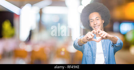 Giovane americano africano uomo con capelli afro sorridente in amore che mostra il simbolo del cuore e la forma con le mani. Concetto romantico. Foto Stock