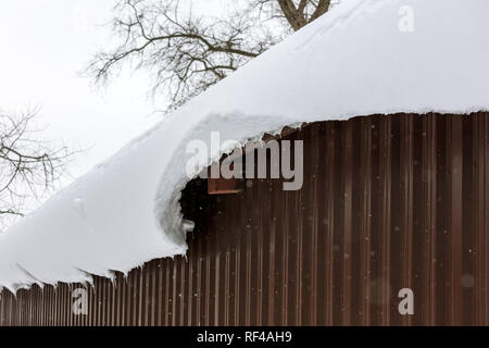 Un enorme blocco di neve pende dal tetto del capannone di metallo. cornicione di neve Foto Stock