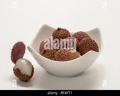 Diversi lychee frutti, in una ciotola bianco accanto ad essa uno con il guscio aperto Foto Stock