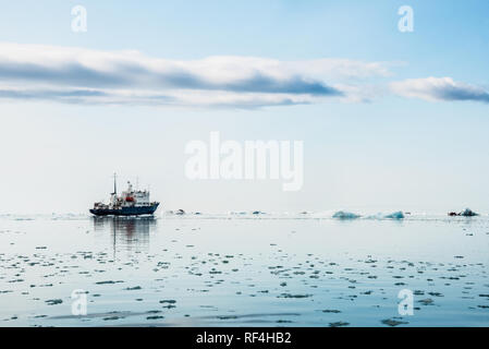 NORDEAUSTLANDET, Svalbard — Una nave da ricerca naviga attraverso le acque ghiacciate vicino al ghiacciaio Bråsvellbreen a Nordaustlandet, Svalbard, Norvegia. Bråsvellbreen è uno dei più grandi ghiacciai di sbocco della calotta di ghiaccio di Austfonna, la seconda calotta di ghiaccio più grande d'Europa. Le Svalbard sono un arcipelago situato nell'Oceano Artico, a metà strada tra la Norvegia continentale e il Polo Nord. La regione è conosciuta per i suoi ghiacciai, le montagne e l'abbondante fauna selvatica, che la rendono un'area significativa per la ricerca scientifica e l'esplorazione polare. Foto Stock