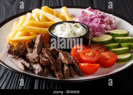 Carni bovine Döner Kebab su una piastra con patatine fritte, insalata e salsa di close-up su di un tavolo di legno. Posizione orizzontale Foto Stock