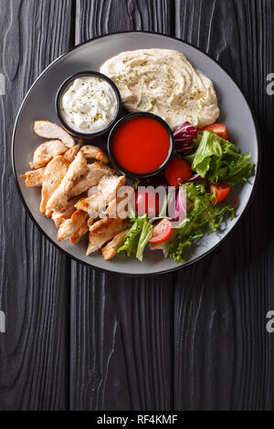 Pollo mediterraneo Shawarma ciotola con hummus, insalata di verdure e salsa di close-up su di un tavolo di legno. Verticale in alto vista da sopra Foto Stock