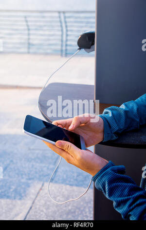 Femmina usando il telefono e la carica su un caricabatteria pubblica Foto Stock