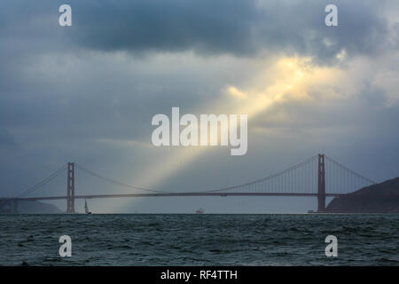 Raggio di sole dorato si rompe attraverso la pioggia nuvole sopra il Ponte Golden Gate e la baia di San Francisco Foto Stock