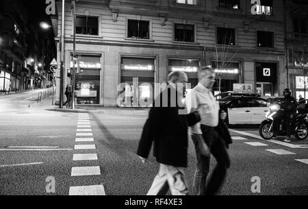 Barcellona, Spagna - Nov 11, 2017: Senior maschio giovane attraversamento strada sulla Via Augusta viale nel centro di Barcellona con la Deutsche Bank office in background - bianco e nero Foto Stock