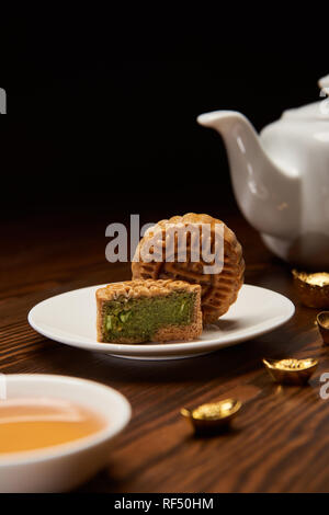 Messa a fuoco selettiva di cinese tradizionale mooncakes, teiera e oro Lingotti su un tavolo di legno isolato su nero Foto Stock