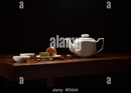 Cinese tradizionale mooncakes, teiera e oro Lingotti su un tavolo di legno isolato su nero con spazio di copia Foto Stock