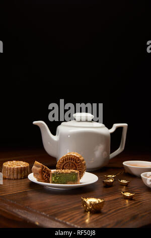 Cinese tradizionale mooncakes, teiera e oro Lingotti su un tavolo di legno isolato su nero Foto Stock