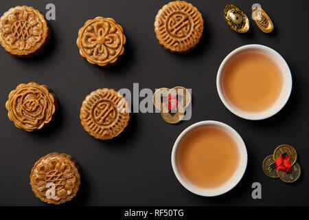 Vista superiore della tradizionale mooncakes, tazze da tè e feng shui monete isolato su nero Foto Stock