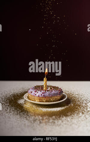 Candela che brucia nel mezzo di una gustosa ciambella con la caduta di scintille isolato su nero Foto Stock