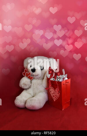 Orsacchiotto di peluche tenendo i cuori e la sacca di custodia di candy baci, con cuore rosso sfondo. Foto Stock