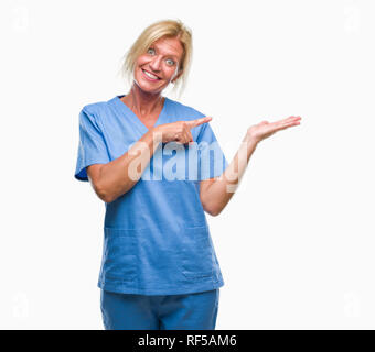 Medioevo donna bionda che indossa medico infermiere uniforme su sfondo isolato stupiti e sorridente alla fotocamera durante la presentazione con la mano e puntamento Foto Stock