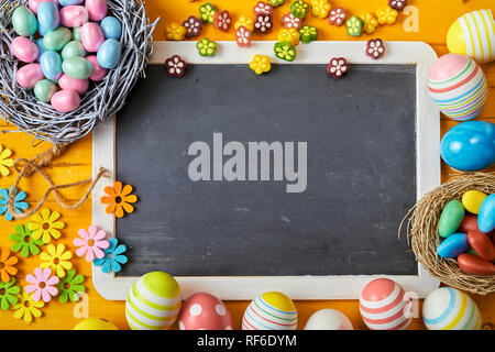 Colorato sfondo Pasqua con uova e decorazioni di fiori simboleggia la molla attorno ad una scuola vuota ardesia con copia spazio per il tuo annuncio stagionali Foto Stock