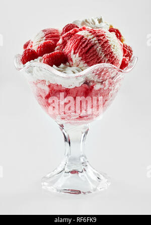 Lampone e gelato alla vaniglia gelato con frutta fresca e panna montata servita in una ciotola di vetro in una vista laterale isolato su bianco Foto Stock